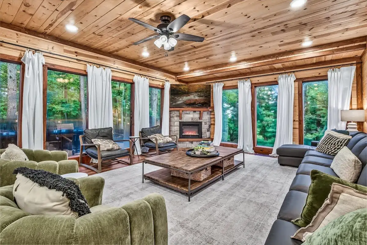 Great room at Blue Smoke Lodge with a stone fireplace, vaulted wood ceiling and mountain-facing windows