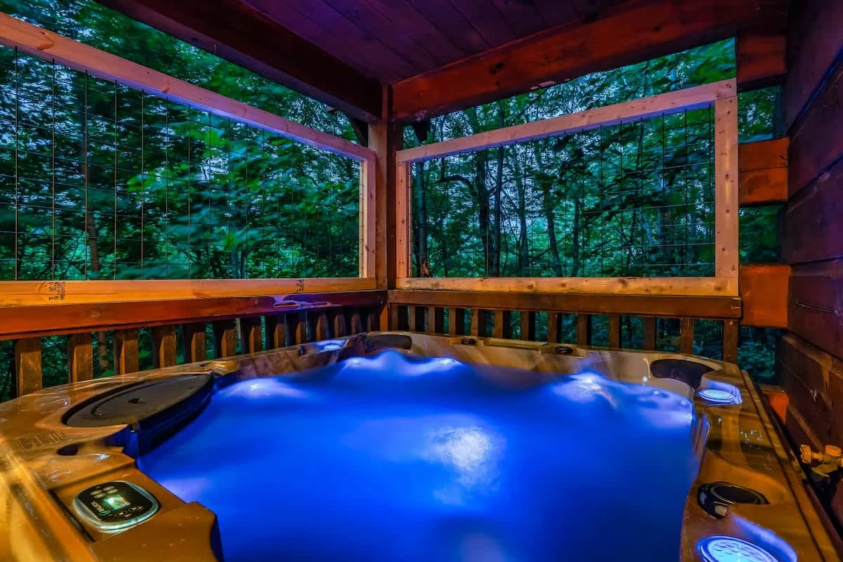 Private hot tub lit blue at night on the covered deck at Break Point Lodge